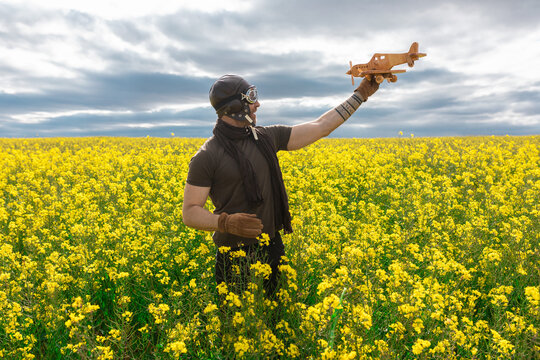 Man in vintage pilot outfit playing with a toy plane in a field