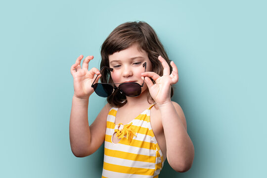 Young girl playing with oversized sunglasses on blue background