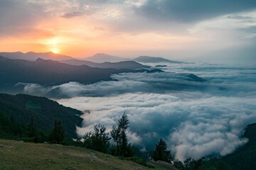 Landscape in which the sun is setting over a valley filled with wispy, low-lying clouds