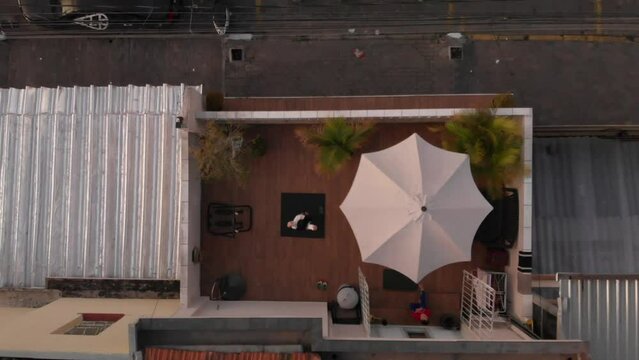 Aerial top view video of a girl meditating on a rug on the roof of a building next to the road