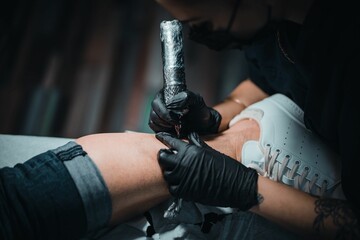 Woman with a tattoo machine in her hand starting giving a tattoo to another person