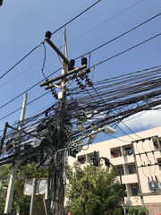 A lot of tangled wires on public utility poles outdoors on blue sky background. Means of...