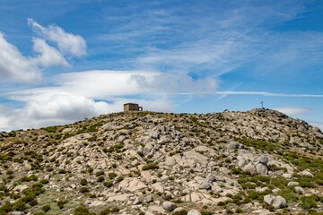Wooden cross atop the peak of a rocky mountain against the cloudy blue sky