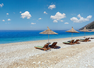Summer morning beach with aquamarine water, sunbeds and strawy sunshades (Albania).