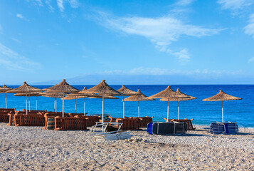 Summer morning pebbly beach with sunbeds and strawy sunshades (Borsh, Albania).