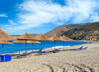Summer morning pebbly beach with sunbeds and strawy sunshades (Borsh, Albania).