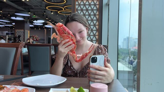 girl eats a large snow crab in a restaurant, examines the huge claws, takes photographs. and writes a blog about the correct cutting of seafood.