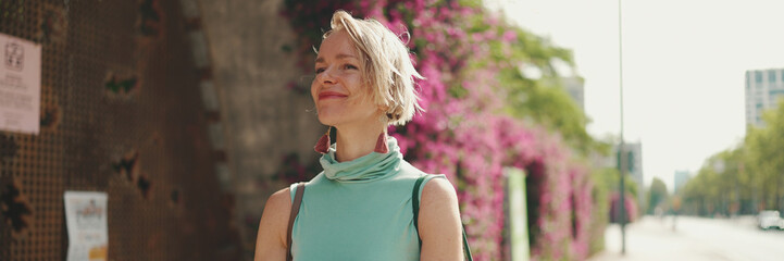 Beautiful happy woman with short blond hair in casual clothes walking down the street, panorama