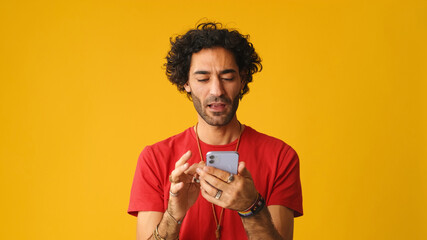 Man with curly hair wearing red T-shirt, using mobile phone gives thumbs up hold in hand do online...