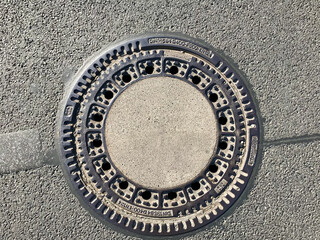 Iron hatch with a pattern above an observation well is located on auto road in daytime. Close-up