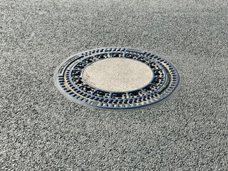 Iron hatch with a pattern above an observation well is located on auto road in daytime. Close-up