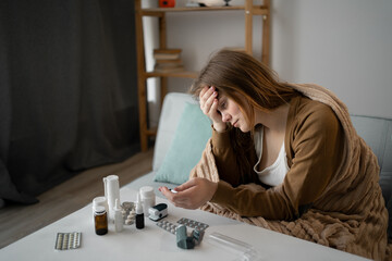 A sick woman is wrapped in blanket on the sofa. Suffering from flu-like symptoms, including...