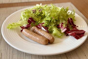 Lettuce and fried sausages in a white plate on the table in the restaurant. A light breakfast to keep fit. Close-up
