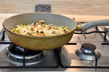 Cellophane noodles, mussels, corn, carrots, bean pods preparing in frying pan on the gas stove at home. Healthy meal food top view in background old kitchen