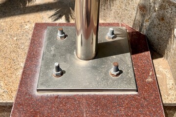 Metal pillar fastened to basement with different anchor bolts and nuts. The support of the iron black pillar on a green lawn in city center