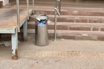 Overflowing trash can and scattered garbage on a sidewalk next to stairs next to supermarket