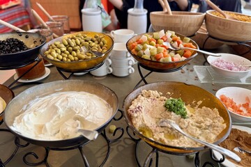 Side view of pickled vegetables as carrots, pickles, corns and green olives, sour cream, sauces in the bowls with a spoons are on the buffet table during lunch. Close-up
