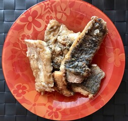 Fried pieces of pollock fish on a red plate on the table in a restaurant, a close-up view from above