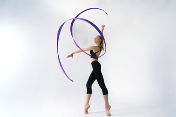 young gymnast in a photo studio shows the elements of exercises with a ribbon, doing stretching and...