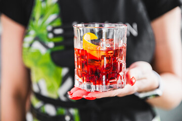 Close-up of hands holding a glass of red cocktail with ice and an orange slice