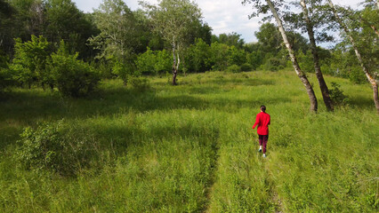a girl in a red sweater runs along the green edge of the forest