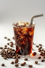 A glass of coffee with a straw in it and a pile of coffee beans on the table