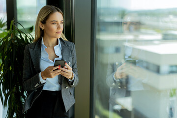 Smiling businesswoman talking on mobile phone by office window in daylight