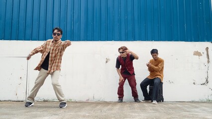 Young street dancer dancing in hip hop style with multicultural friends cheering behind at wall....