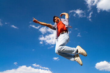 A man is jumping in the air with his arms outstretched. The sky is blue and there are clouds in the...