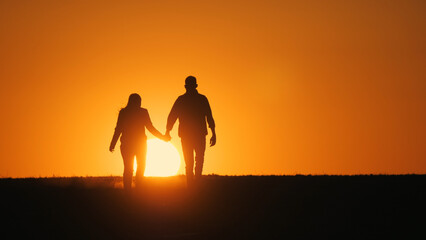 Silhouettes of a young couple walking side by side towards a picturesque sunset