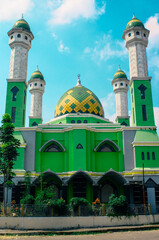 Green mosque with trees in the yard and bright blue sky