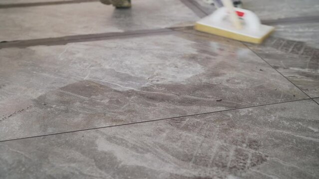 Grouting joints after laying large-format tiles on the floor. Laying floor tiles, cleaning the tiles after filling the joints by the tiler. The tiler wipes down the tiles after laying them.
