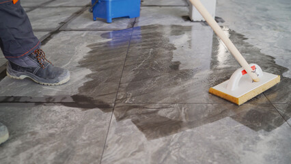 Laying floor tiles, cleaning the tiles after filling the joints by the tiler. The tiler wipes down...