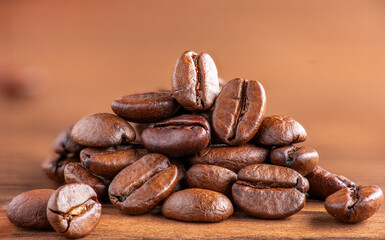 A group of coffee beans close-up on a light brown wooden background.