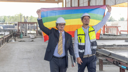 Two engineers with safety hat hold a flag to express their support to LGBT right in a construction...