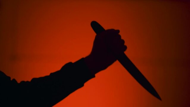 Hand holding knife and stabbing against red background