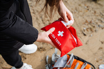 A womans gesture on the beach holding a red first aid kit contrasts with the carmine landscape,...