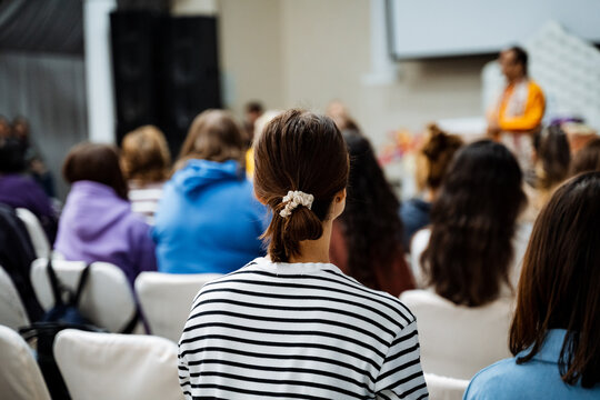 A crowd is gathered in a buildings lecture hall, sharing a presentation. The audience is seated, watching the event. Its a job meeting