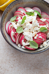 Salad with fresh radish, feta cheese and green basil, vertical shot on a beige stone surface, closeup