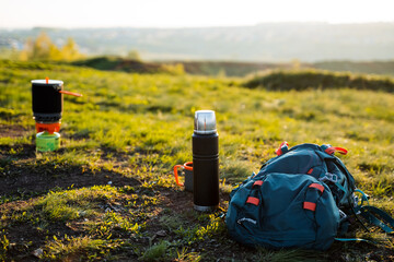A backpack and a thermos are resting on the grass in a highland field, blending into the natural...