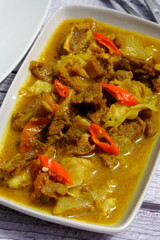 tongseng  is a traditional Indonesian dish made from beef or mutton, spices, coconut milk, cabbage, tomatoes, and chili. Tongseng on a wooden table with vegetables and tomatoes. Indonesian food.