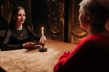 Back view of unrecognizable female client getting divination session with tarot cards at dark...