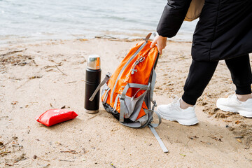 A person standing on the beach with a backpack and a thermos, enjoying the landscape and geological phenomenon. Water, sand, and fun activities are part of their recreation on this travel adventure