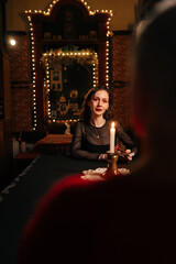 Vertical portrait of fortune teller making tarot layout on table to unrecognizable client when predicting future in dark room by light of burning candle. Concept of prophecy, prediction and esoteric.