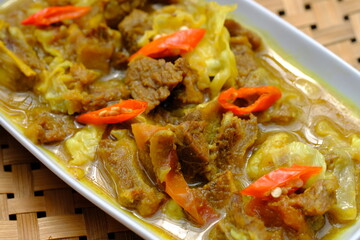 tongseng  is a traditional Indonesian dish made from beef or mutton, spices, coconut milk, cabbage, tomatoes, and chili. Tongseng on a wooden table with vegetables and tomatoes. Indonesian food.