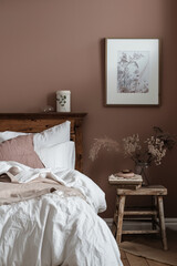 A bedroom wall is painted in a dusty rose color, the bed is made with white linen and has an old wooden headboard, and there is some framed art on one of the walls.