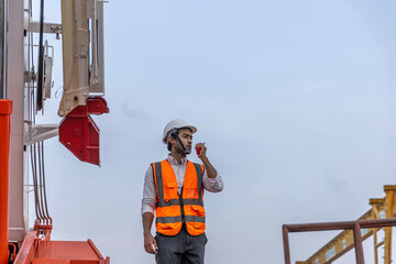A foreman in safety vest is using walkie talkie to communicate with his colleagues in a...
