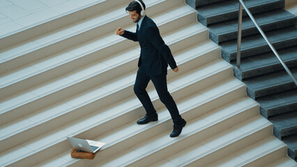 Professional business man standing at stair while moving to music from headphone. Skilled project...