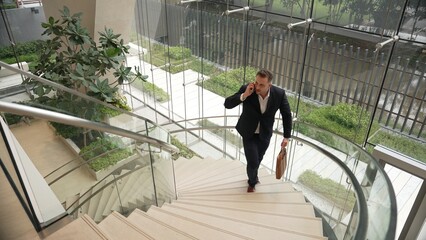 Smart businessman walking up spiral stair case and calling manager by using smart phone. Top view...