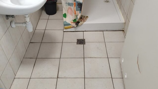 Dirty tiled bathroom with shower and sink and dirty floor in a cheap hostel or student dormitory